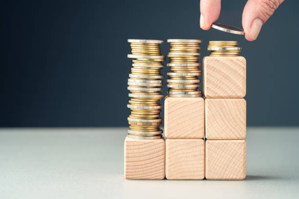 c6 Hand add a few coins at the top of the final level built with wood cubes as step stairs, paying less in the long term, reducing cost, saving for the future, insurance, and investment, or subsidy money concept